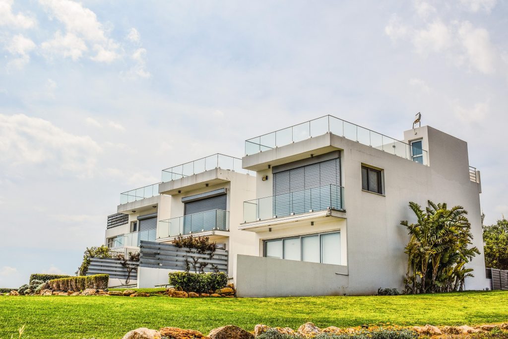 Luxury modern white house with flat roof, glass balconies, and Mediterranean landscaping.